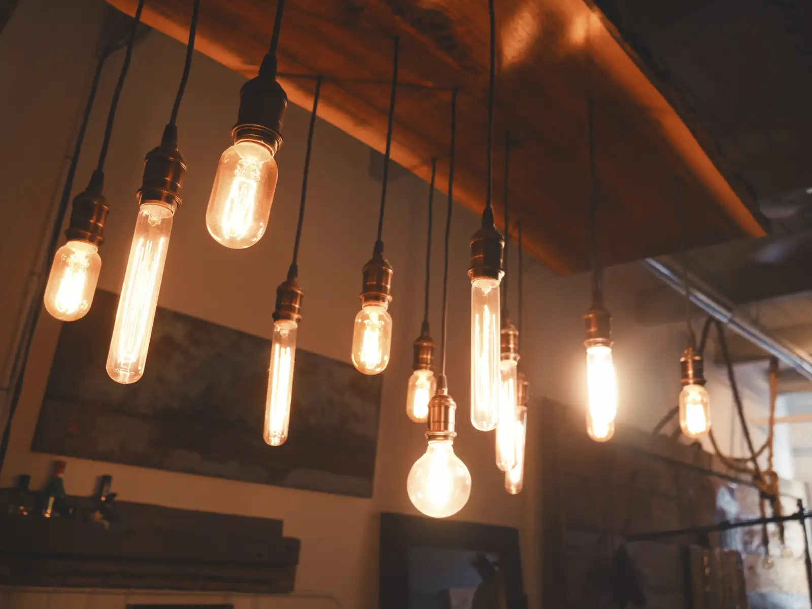 Filament light bulbs hanging on black cords below a wooden beam