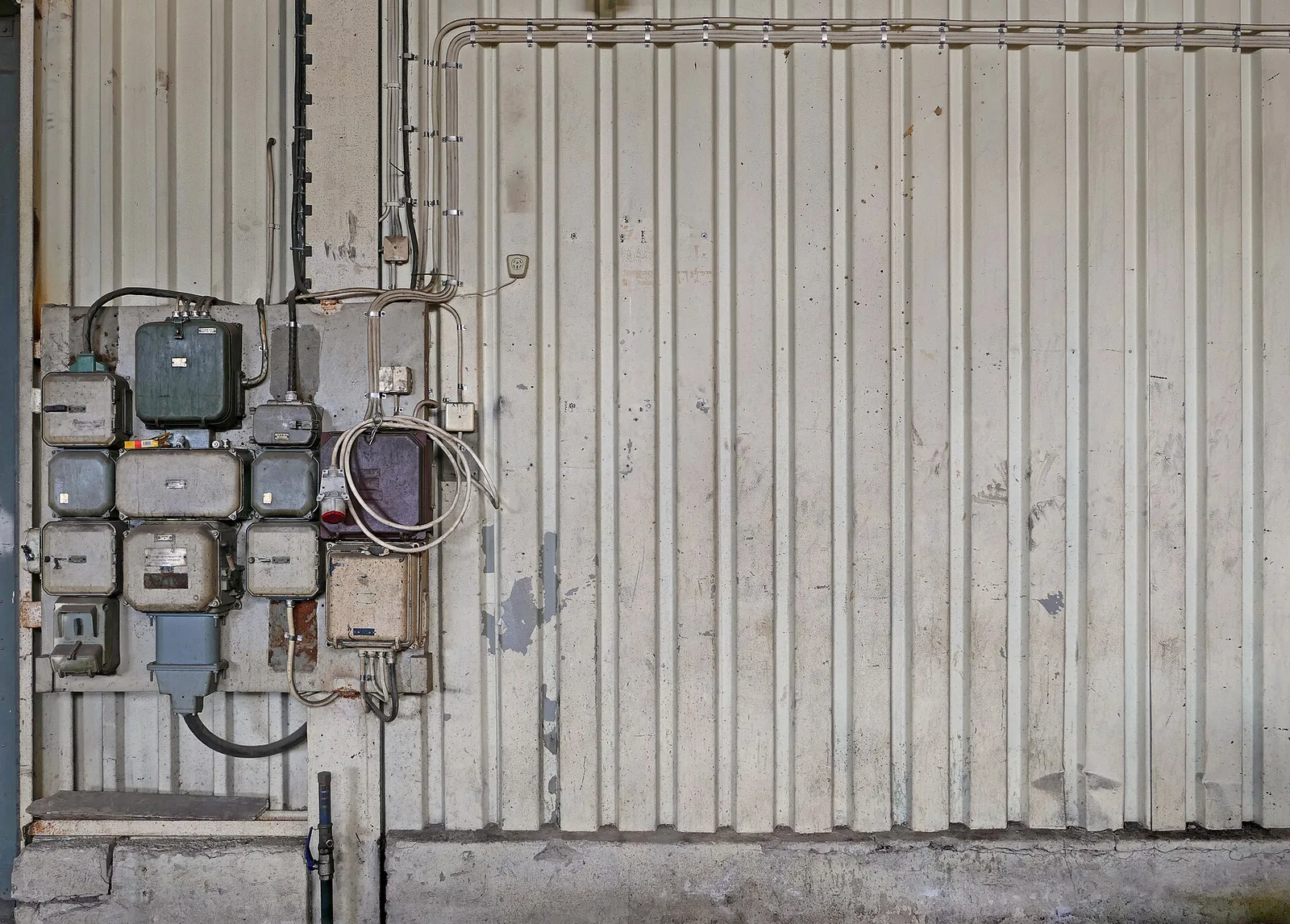 Old metal electrical boxes and conduit on a ribbed metal wall